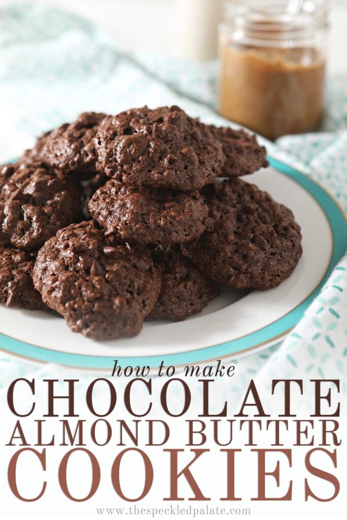 A turquoise-rimmed plate holds a stack of chocolate almond oat cookies sitting on a patterned aqua and white towel with a jar of almond butter and a glass of almond milk behind it with the text 'how to make chocolate almond butter cookies'