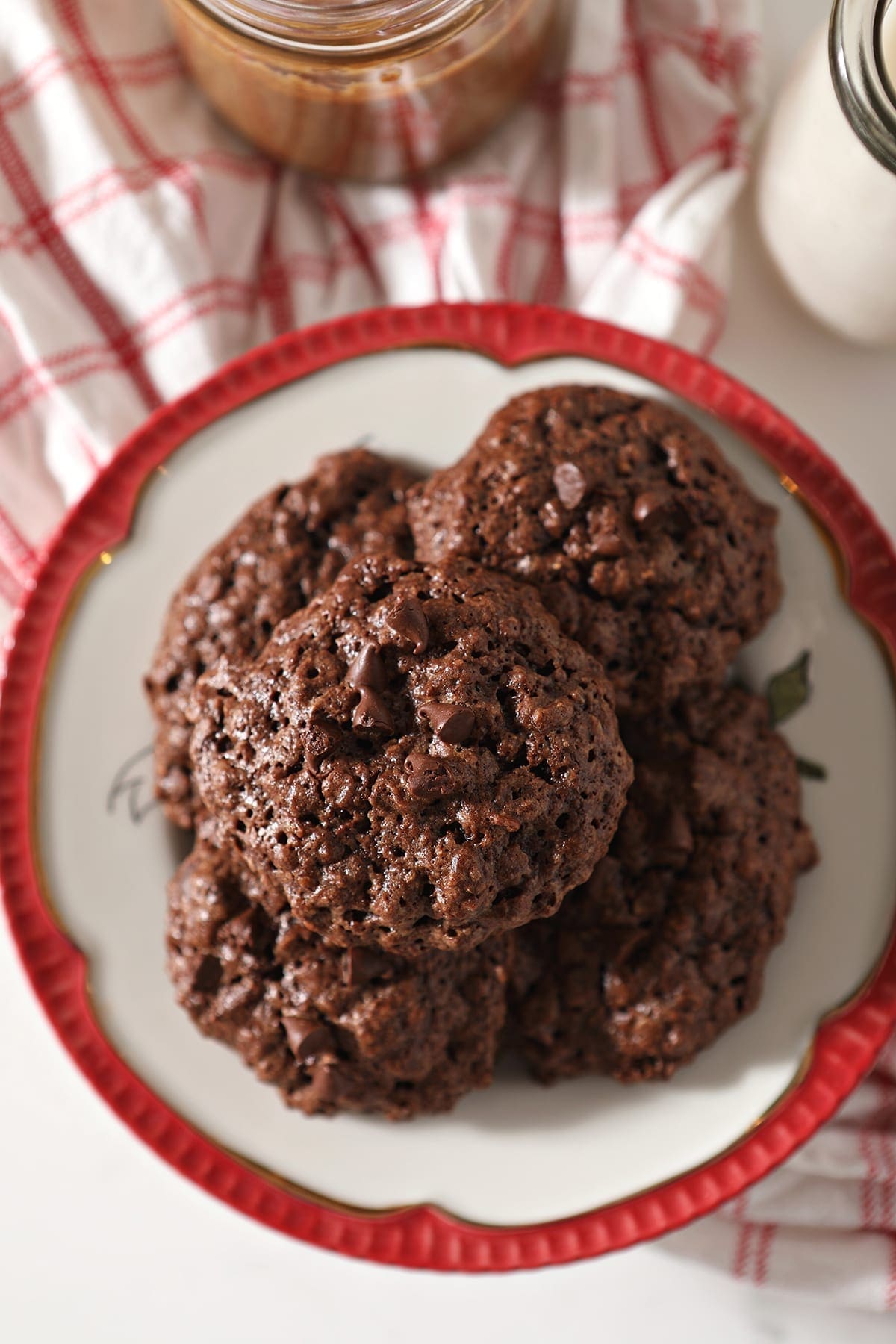 Close up of Chocolate Almond Butter Cookies with Chocolate Chips on a red-rimmed plate sitting on a red plaid towel