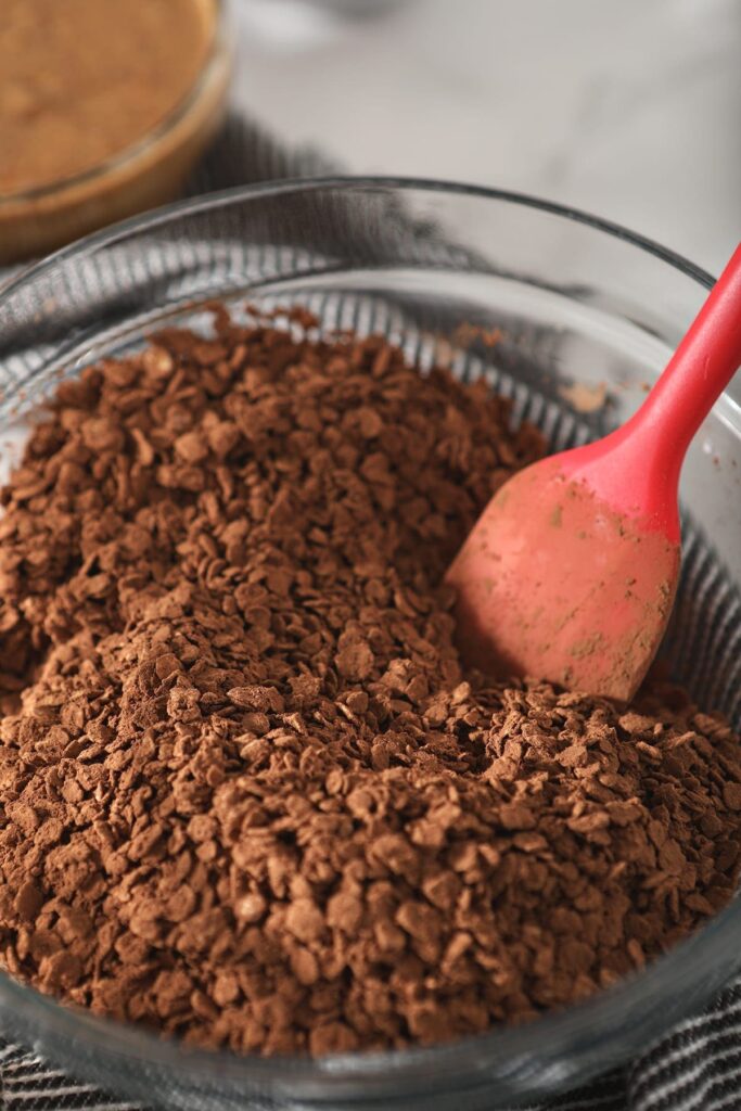 Rolled oats coated in cocoa powder sit in a bowl with a red spatula