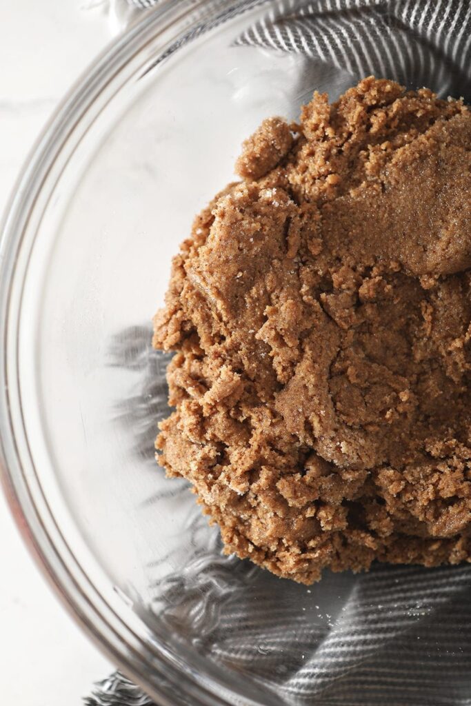 Close up of almond butter and sugar mixed together in a clear glass bowl sitting on a gray and white striped towel