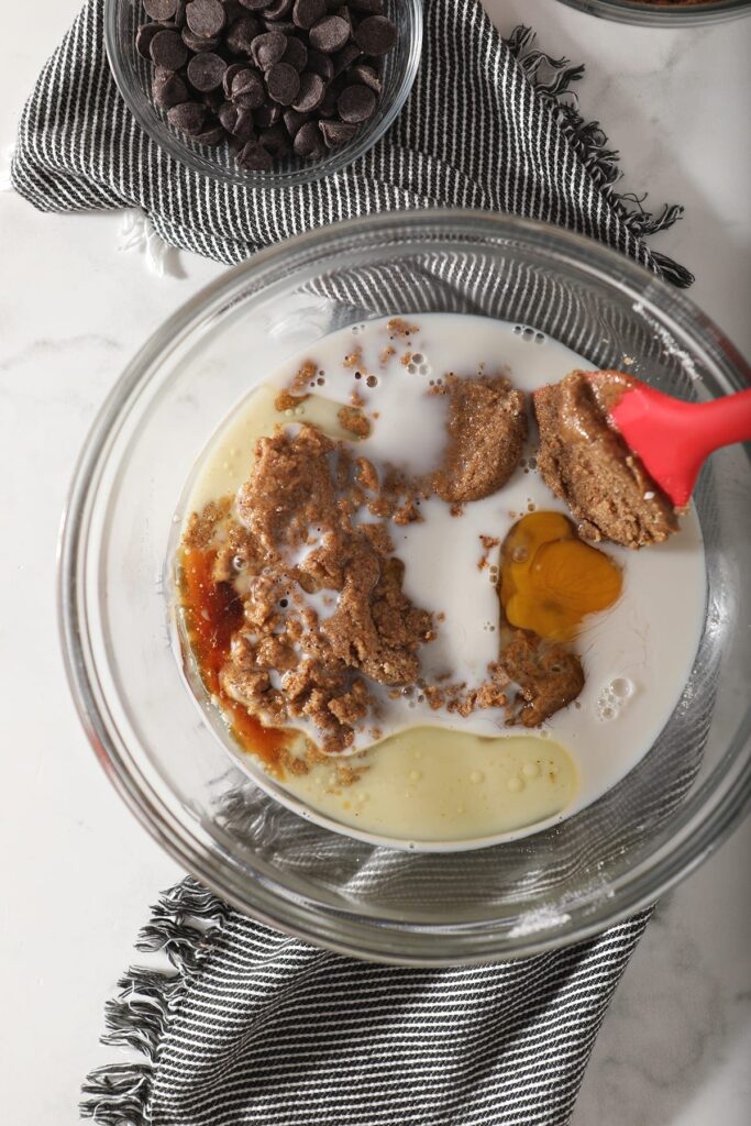 Almond milk, oil, vanilla, egg and the sugar-almond butter mixture in a large glass bowl with a red spatula before mixing