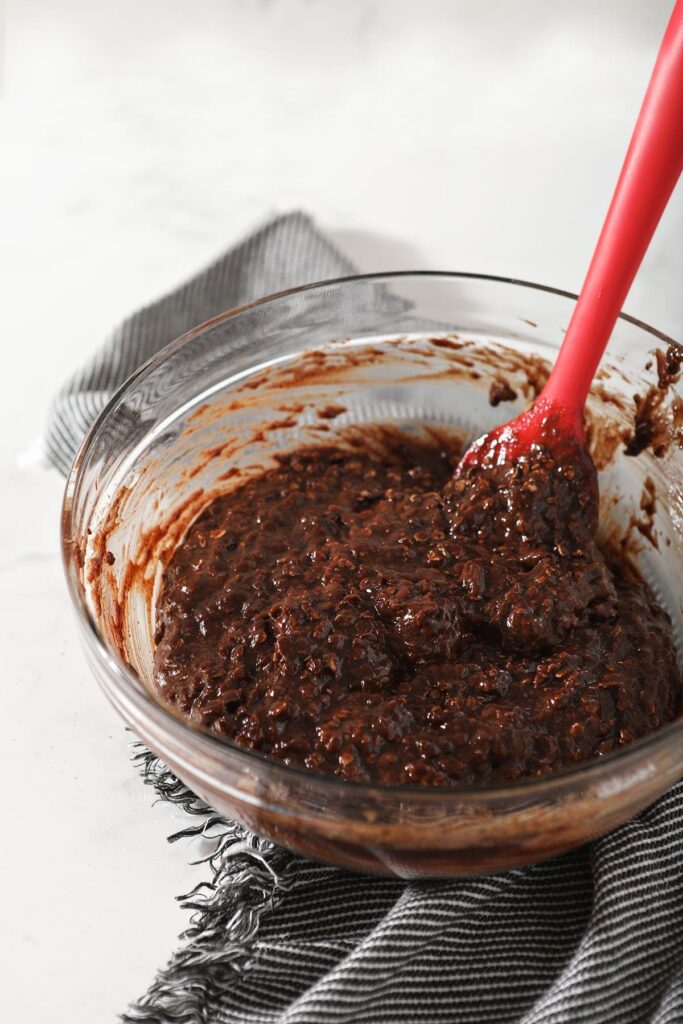 The gluten free cookie batter in a clear glass bowl with a red spatula on top of a gray and white striped towel