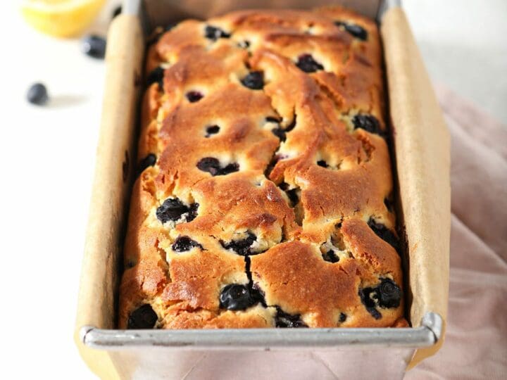 A loaf of Lemon Blueberry Bread in a loaf pan on marble