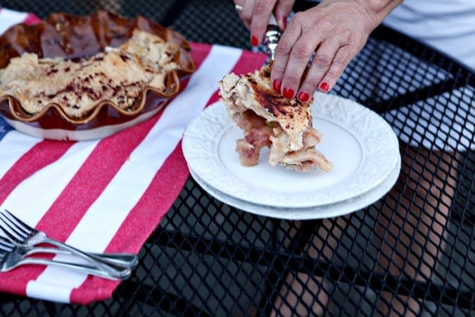 A light skinned woman with red fingernails serves a slice of pie on a white plate