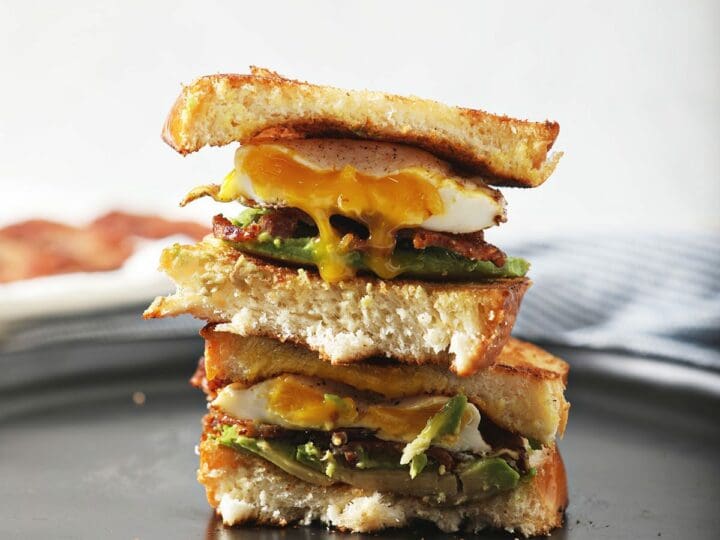 A halved Bacon Avocado Egg Sandwich on top of itself on a black plate