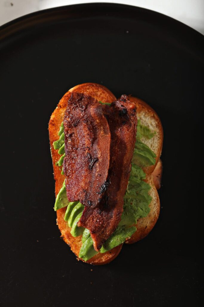 Crispy bacon on avocado on toast on a black plate