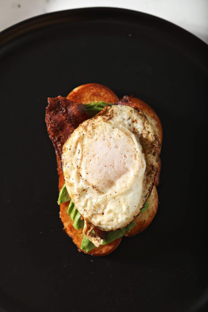 A fried egg on top of bacon, avocado and toast