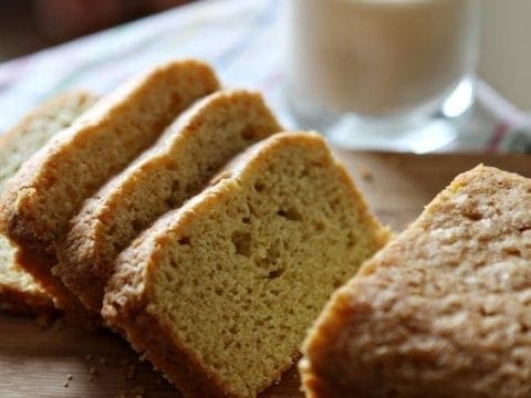 Sliced pound cake on wood board next to glass of milk