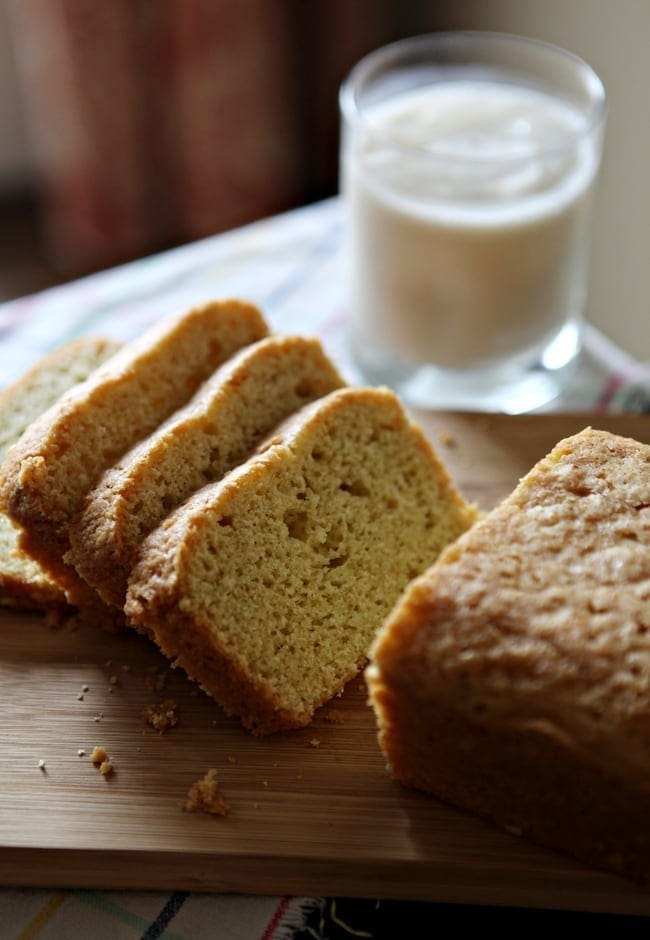 Sliced pound cake on wood board next to glass of milk 