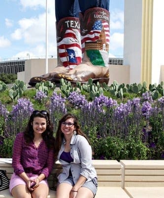 Two woman sitting on a bench smiling in front of flowers