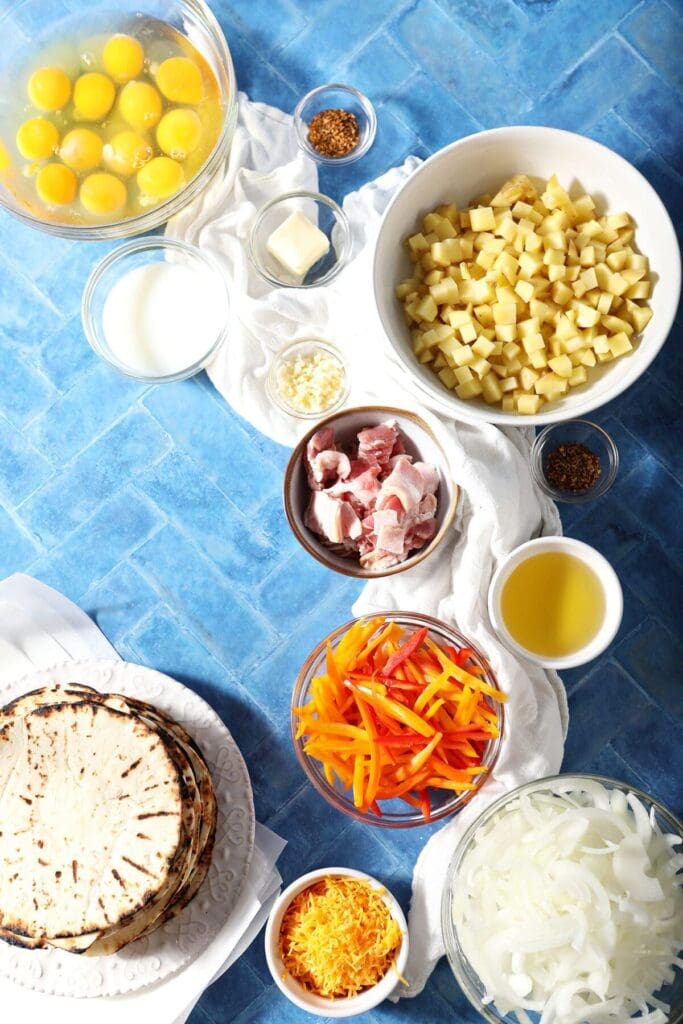 Ingredients to make breakfast tacos in bowls on a blue surface