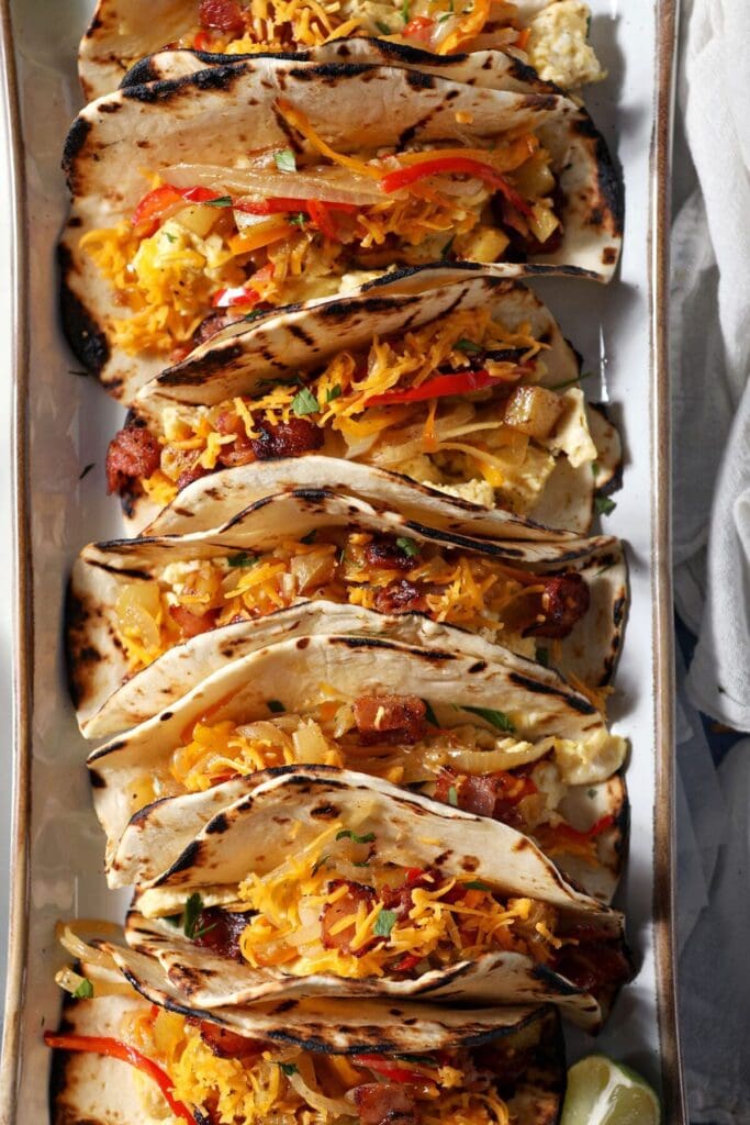 Close up of breakfast egg tacos with bacon, potatoes and veggies on a platter