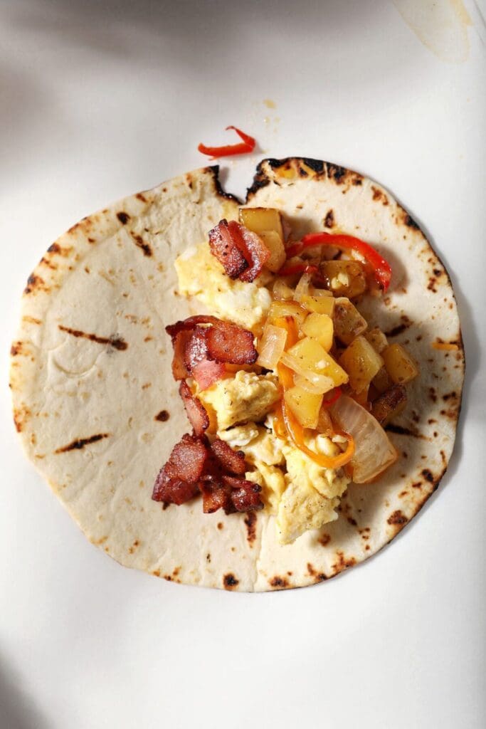 Bacon on top of a breakfast egg taco on a sheet of parchment