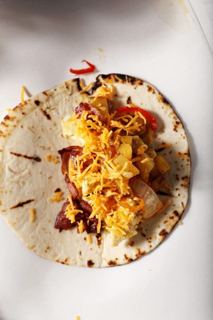 Shredded cheese on top of a breakfast taco on parchment paper