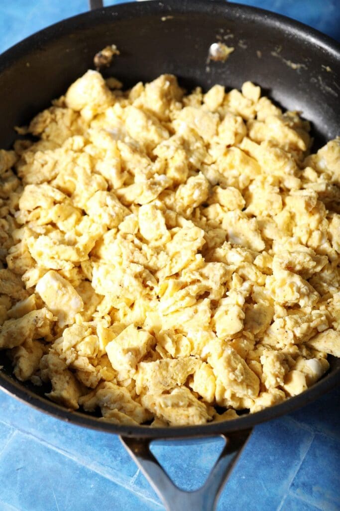 Scrambled eggs in a skillet on a blue surface