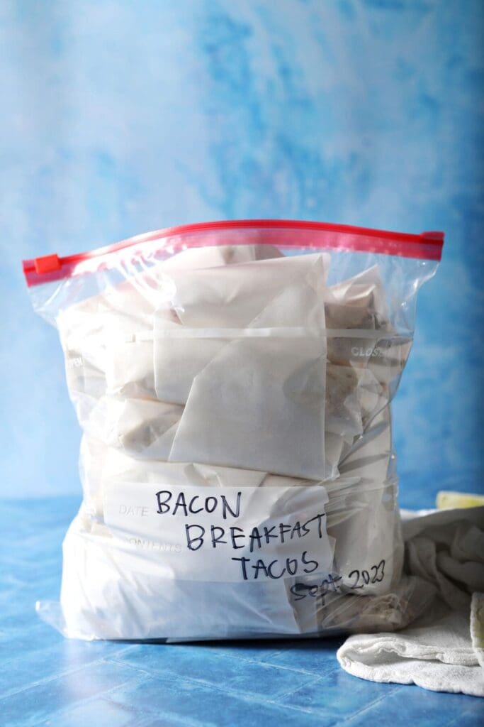 A bag of wrapped bacon breakfast tacos before freezing on a blue background