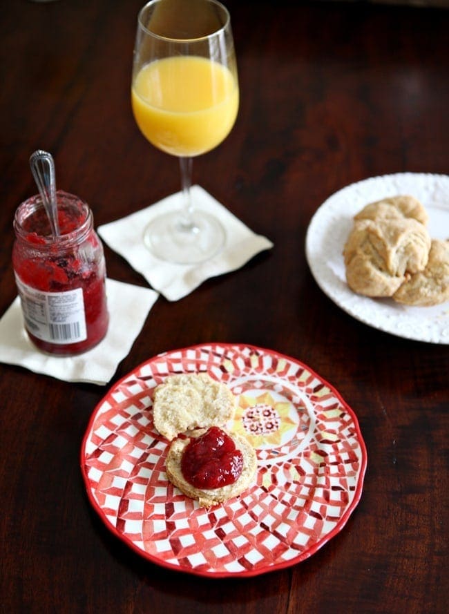 Overhead of a vegan biscuit with red jam on a patterned red plate on top of a dark tabletop