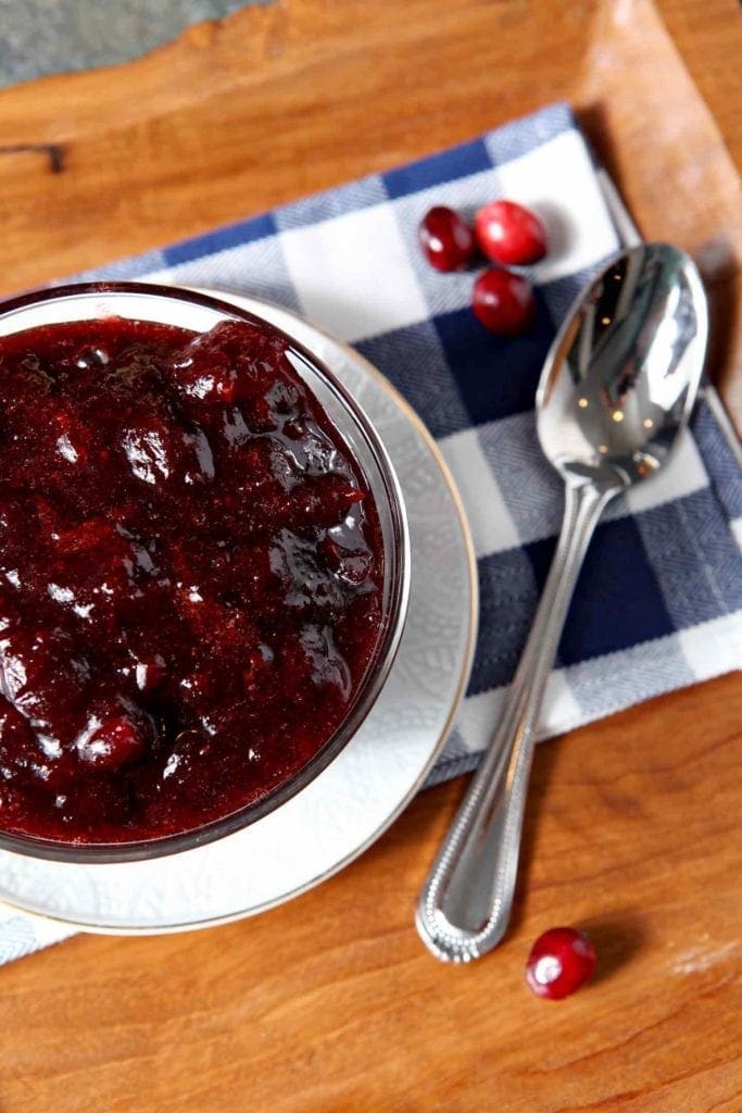 Close up of a bowl of Drunken Cranberry Sauce, shown with fresh cranberries and a serving spoon