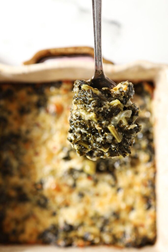 A spoon holds a serving of kale Madeline over a baking dish