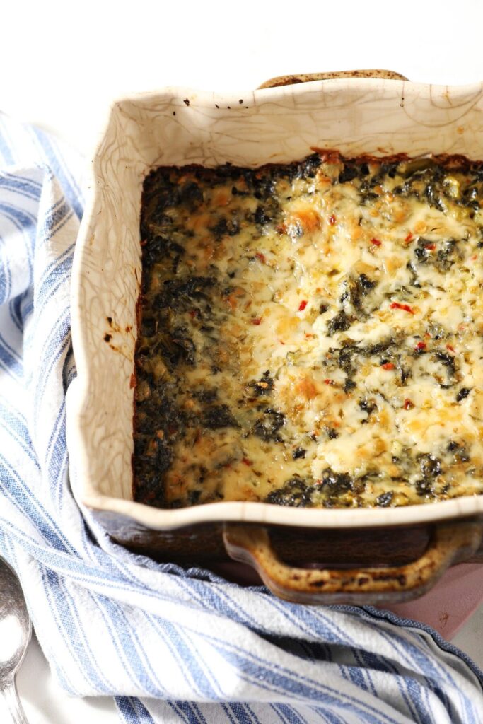 A casserole dish of kale Madeline with a blue striped towel