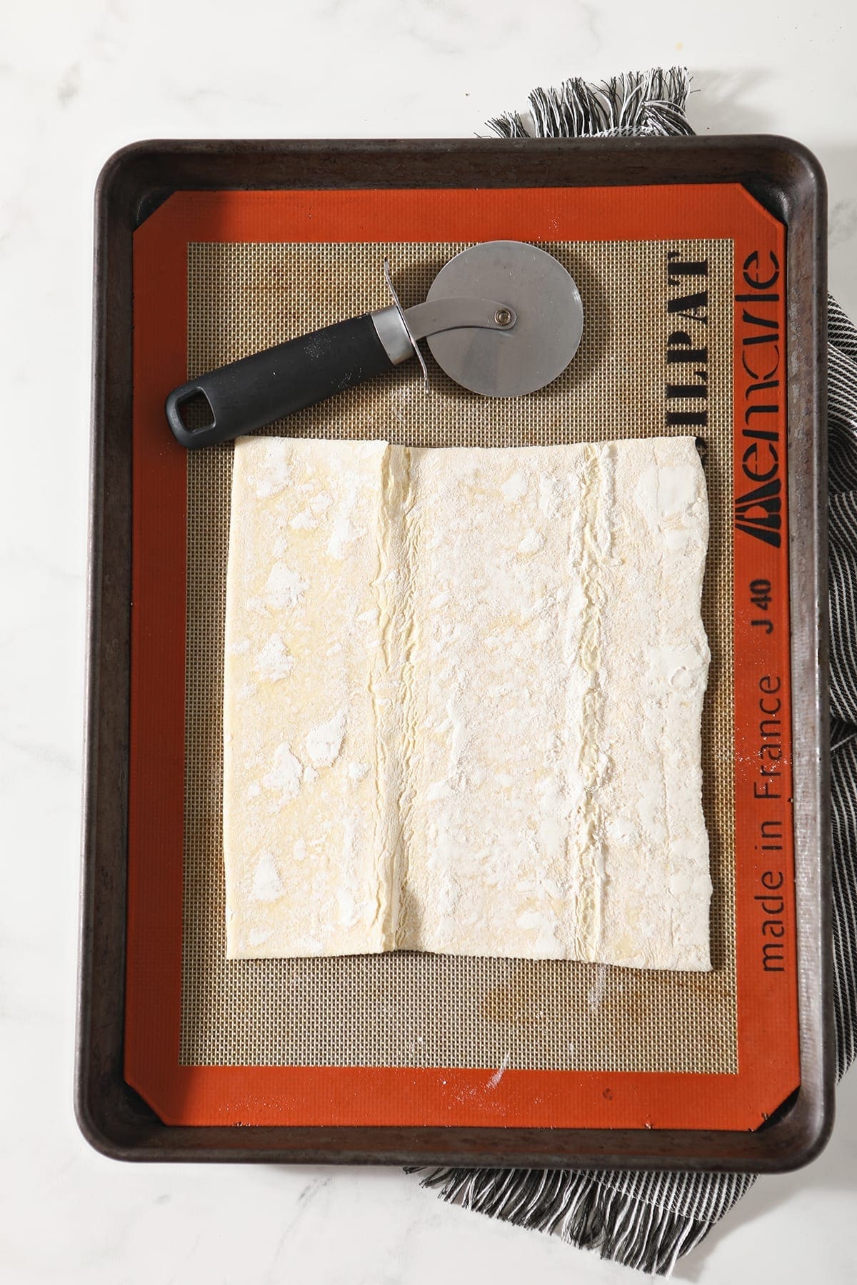 A sheet of puff pastry on a Silpat-lined baking sheet with a pizza cutter