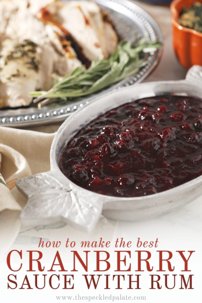 Cranberry sauce in a silver bowl with leafs on the ends next to a silver platter of turkey with the text 'how to make the best cranberry sauce with rum'