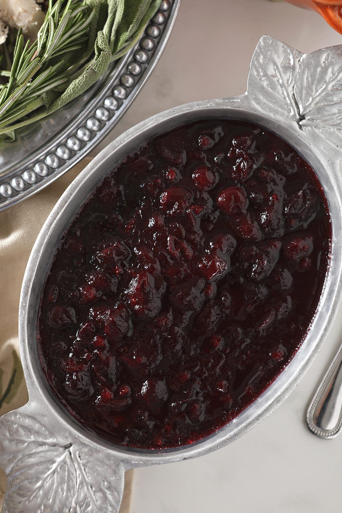 Close up of chilled spiced cranberry sauce in a silver serving bowl with maple leafs on the corners