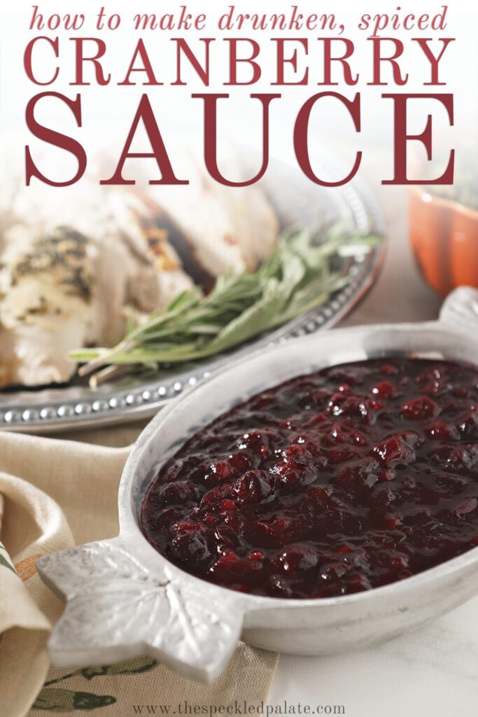 Cranberry sauce in a silver bowl with leafs on the ends next to a silver platter of turkey with the text 'how to make drunken, spiced cranberry sauce'