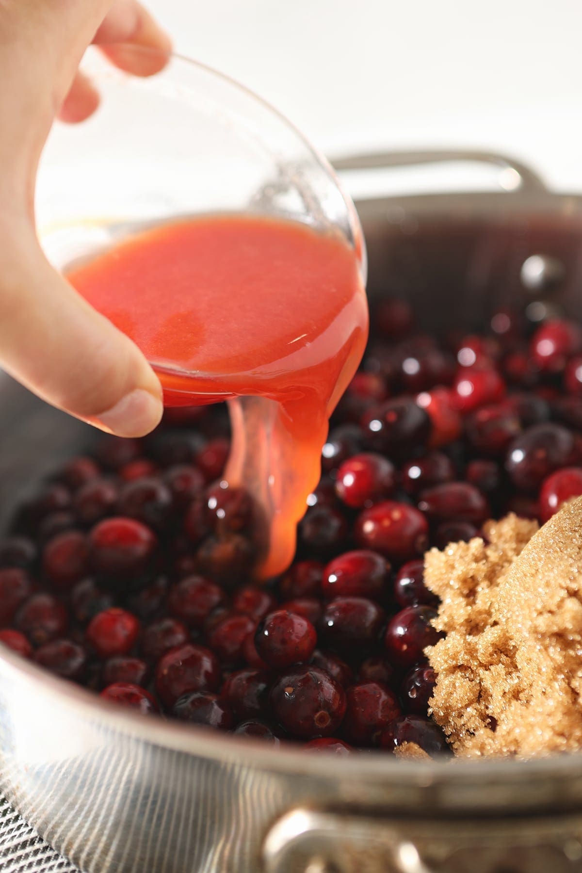 pouring liquid into a pot with cranberries and sugar