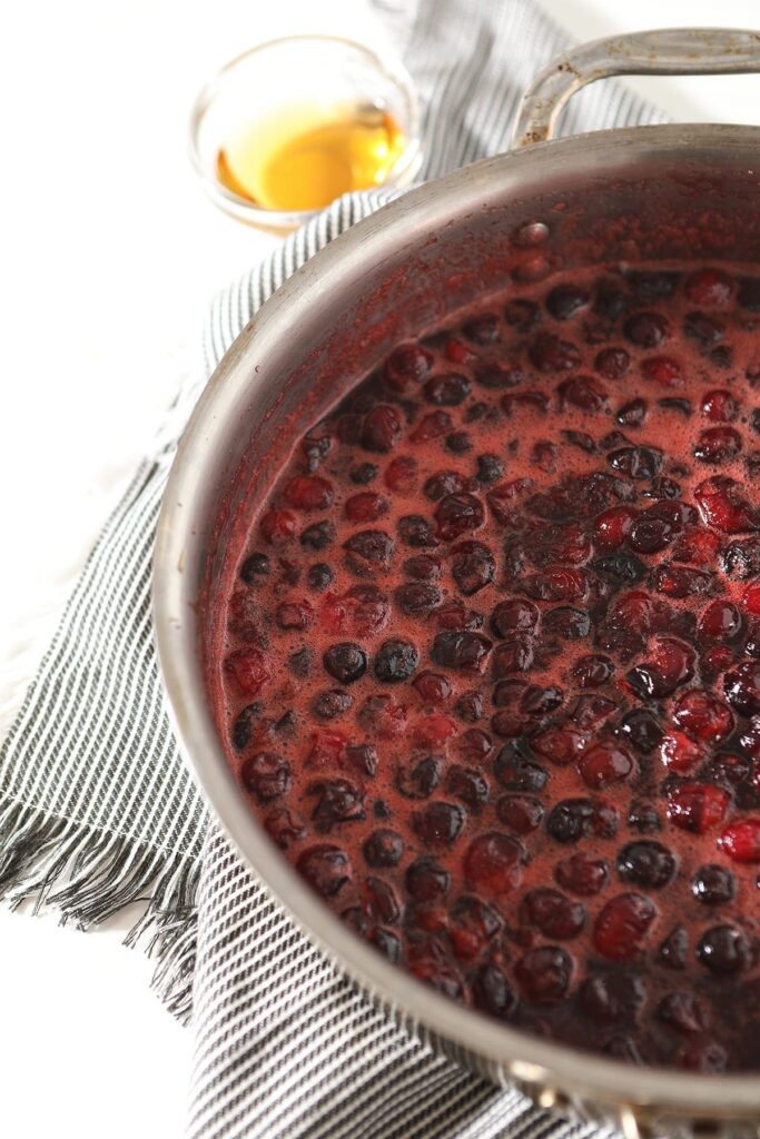 Cranberries bubble in a skillet on a gray towel