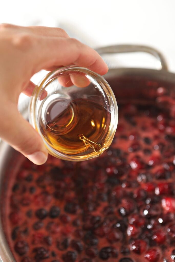 A hand pours rum into bubbling cranberry sauce