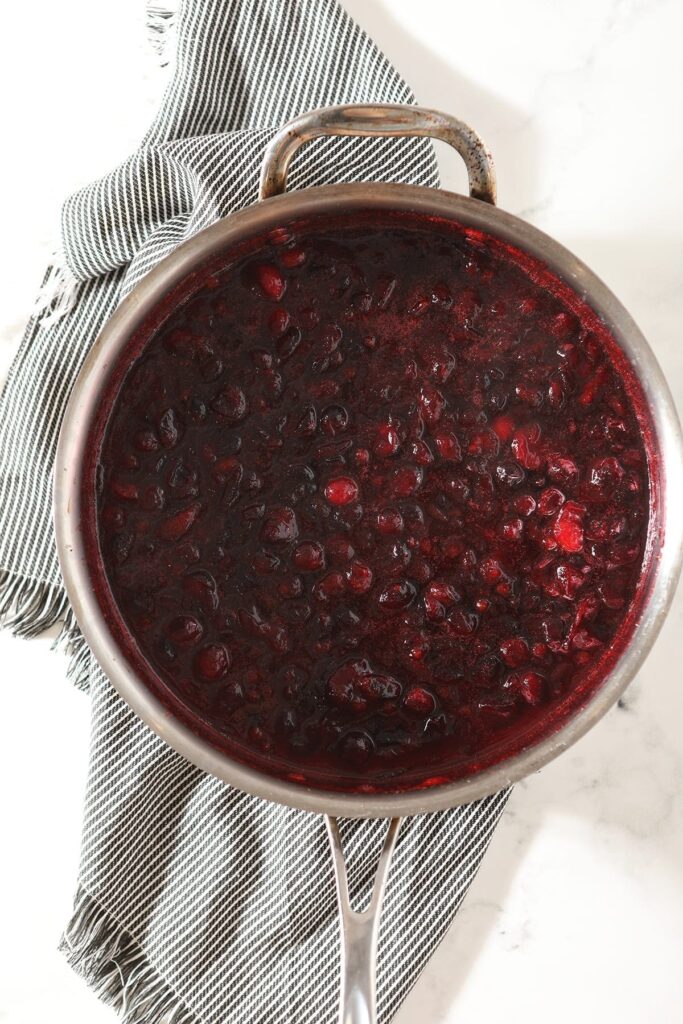 Hot cranberry sauce in a skillet on top of a gray striped towel