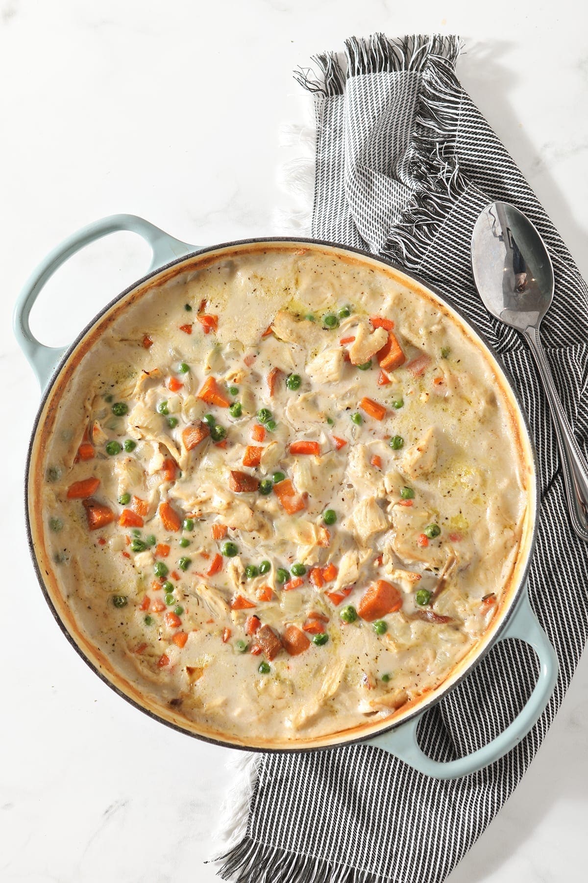 A dish holds turkey pot pie after baking in the oven on top of a striped gray towel with a large serving spoon