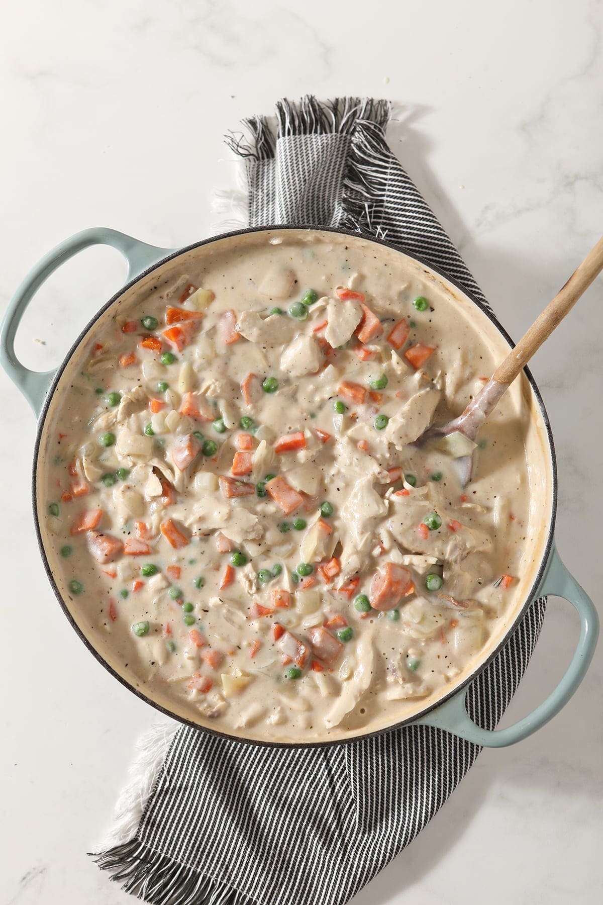 A casserole dish with turkey pot pie inside it sits on a gray striped towel before baking