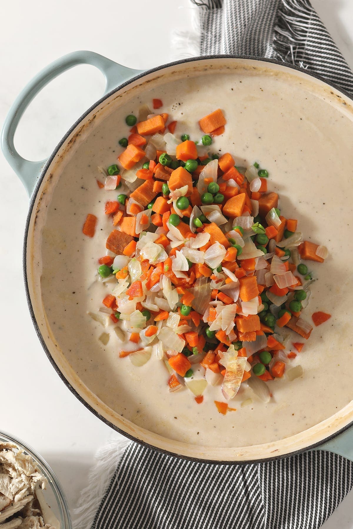 Boiled vegetables sit on top of the pot pie liquid before stirring in to the Dutch oven