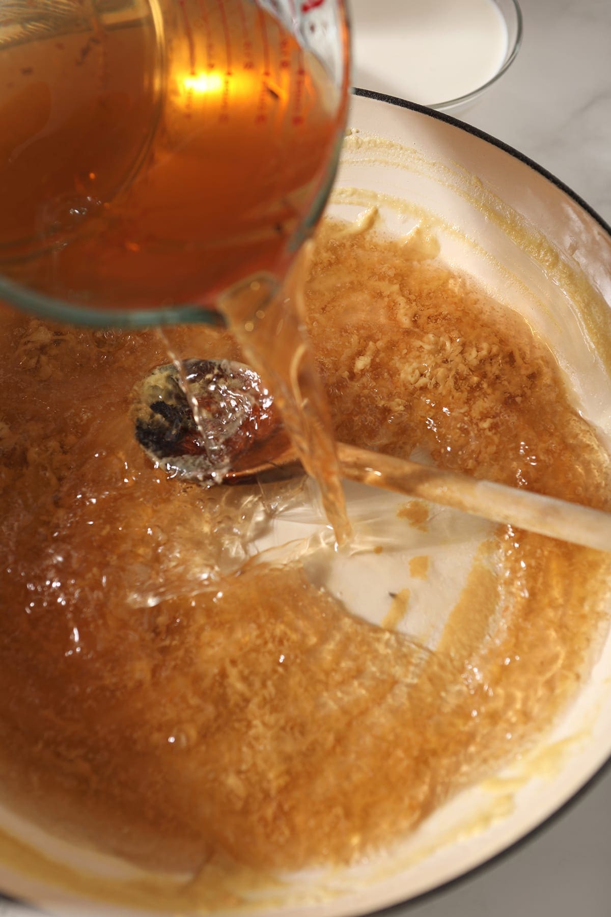 Vegetable stock pours into a Dutch oven with a roux in it