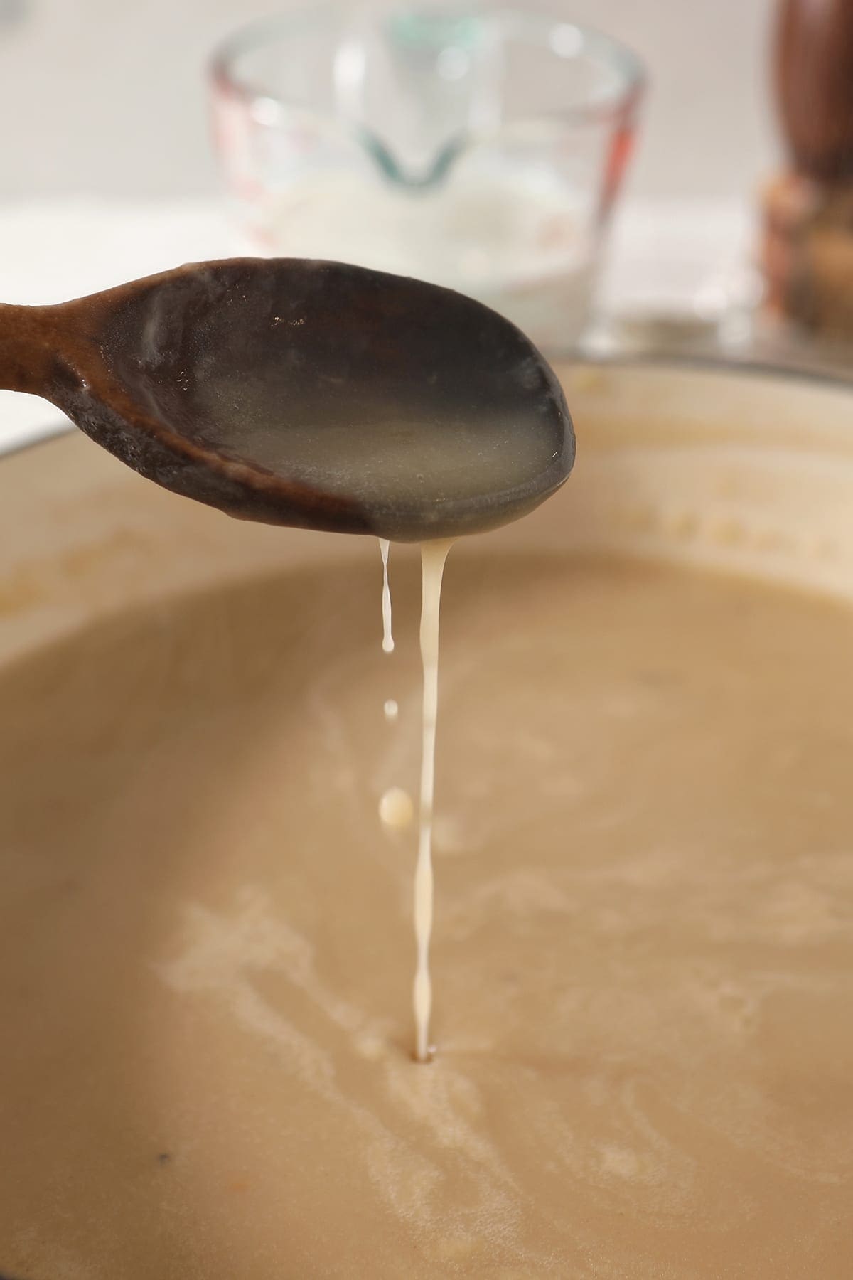 A wooden spoon drizzles a vegetable stock-roux mixture from it