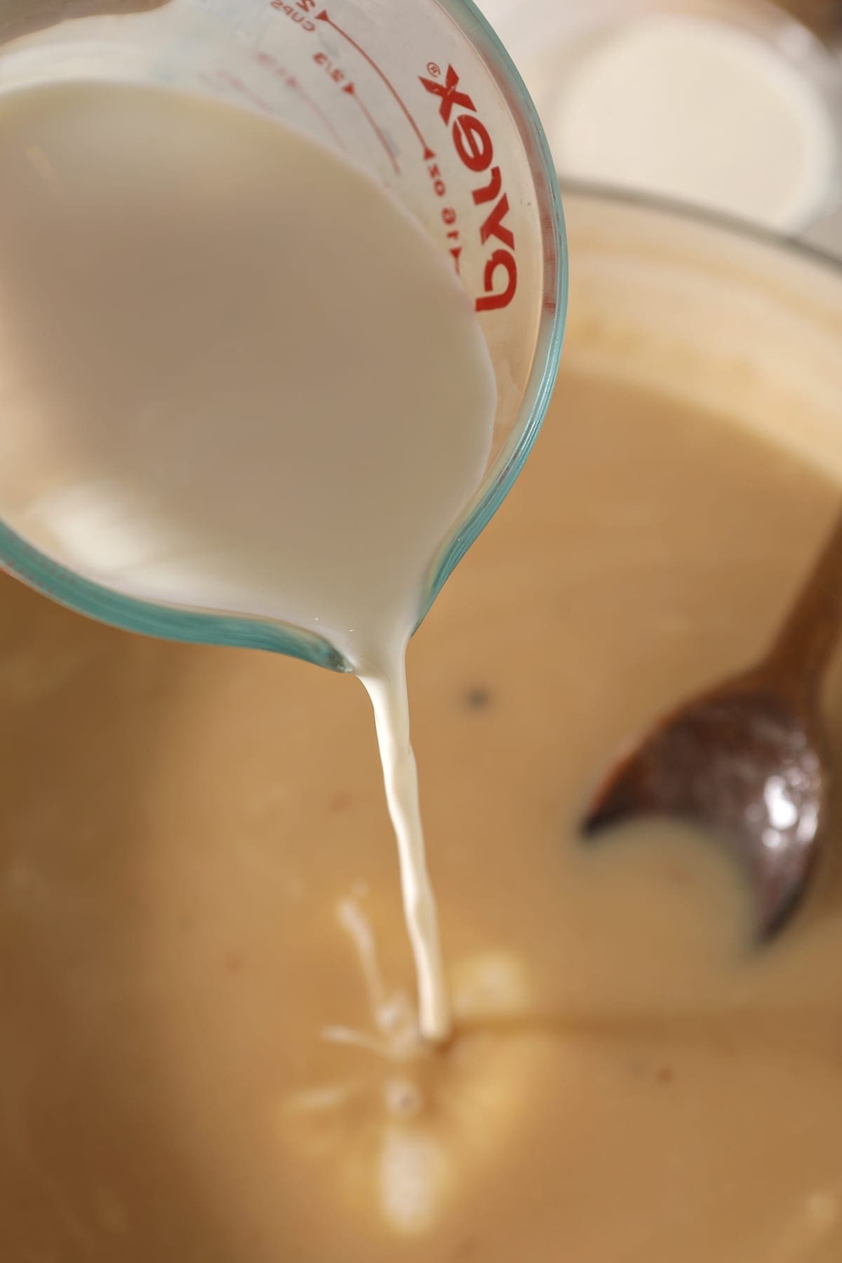 Milk pours into the Dutch oven from a glass measuring cup