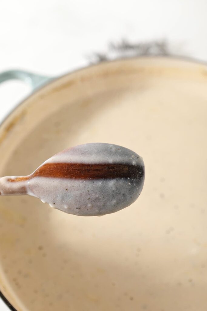 The back of a wooden spoon has a stripe down the back of it, showing the consistency of the pot pie liquid before the vegetables and meat are added