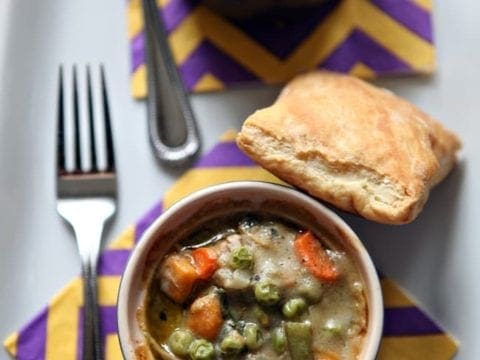 Close up of two mini turkey pot pies from above on yellow and purple striped napkins with forks and puff pastry squares beside them