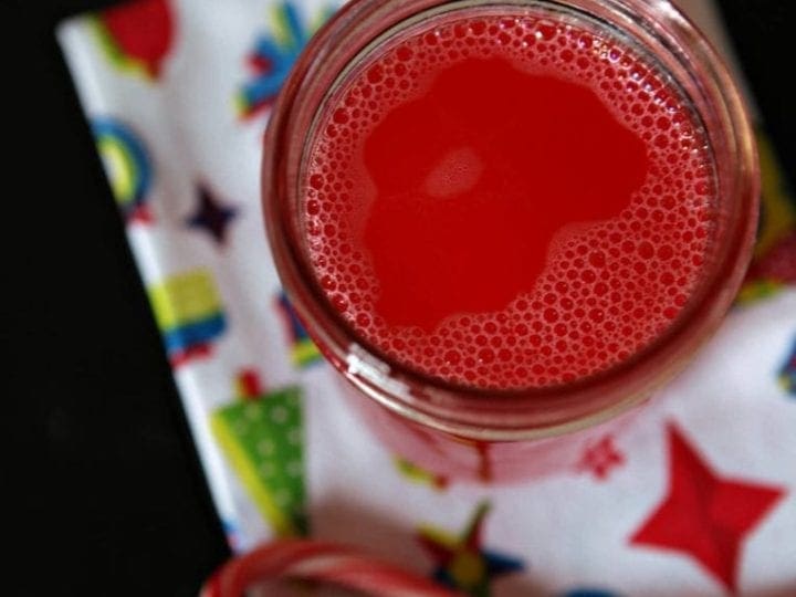 A jar of infused Peppermint Vodka sits on a holiday cloth with candy canes surrounding it