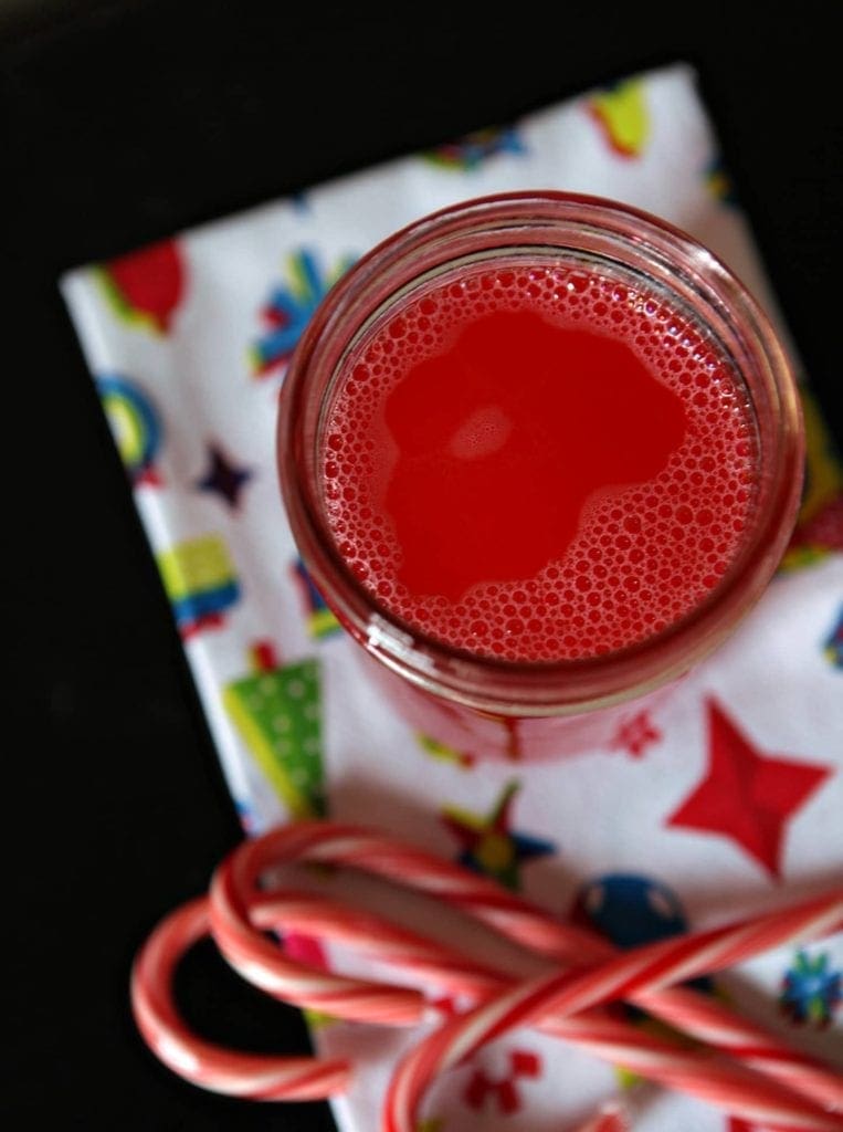 A jar of infused Peppermint Vodka sits on a holiday cloth with candy canes surrounding it