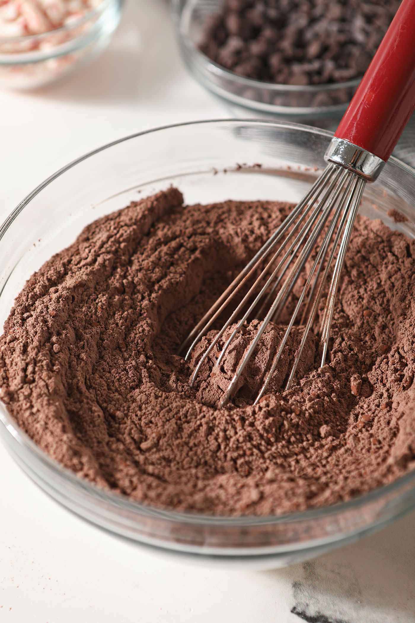 A whisk sits in a bowl with dry ingredients to make chocolate cookies