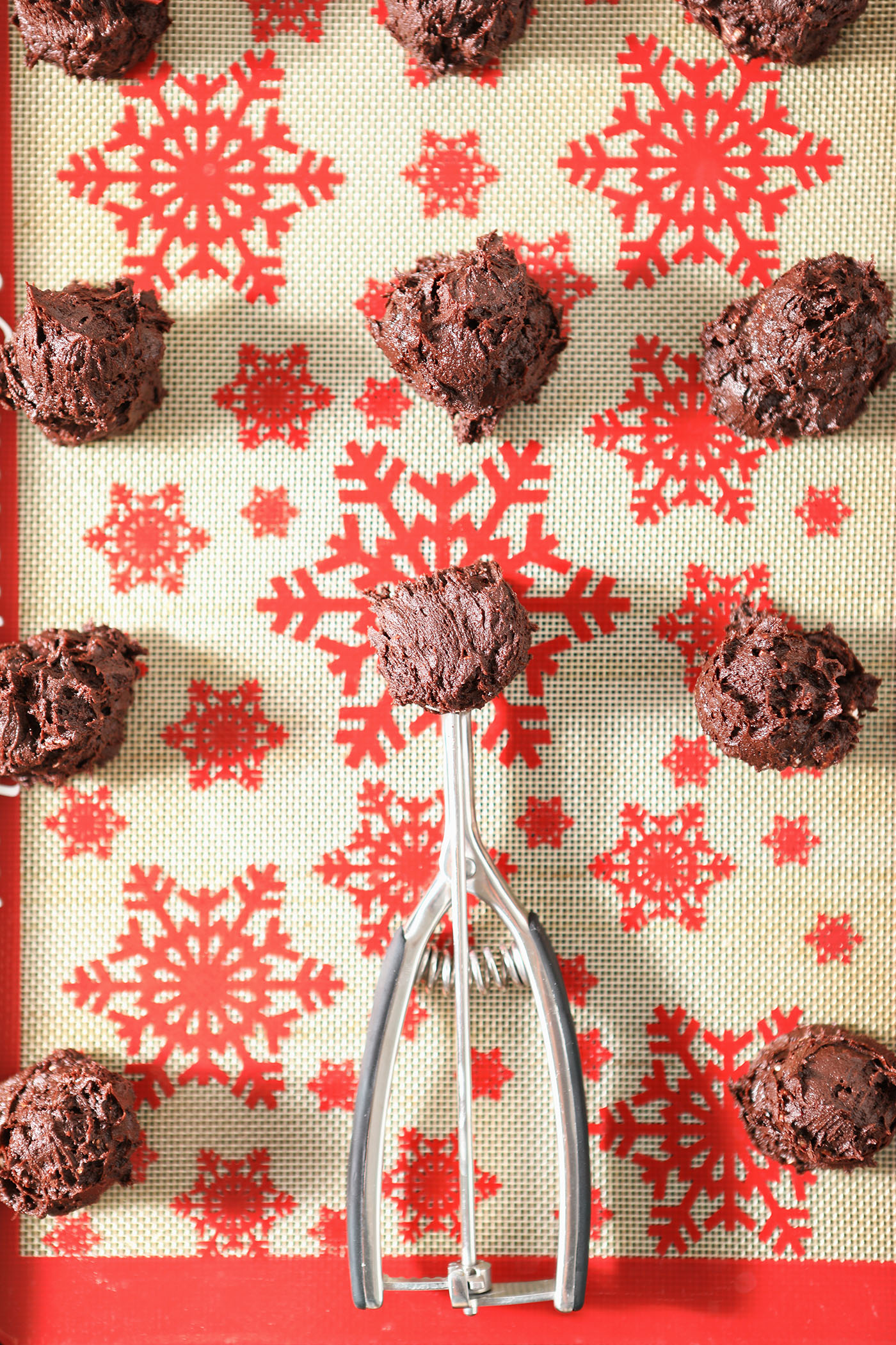 A cookie scoop on a snowflake-printed silicone mat with scoops of chocolate cookie dough