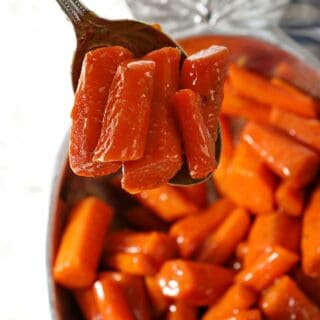 A spoon holds a serving of carrots over a bowl of brown sugar glazed carrots