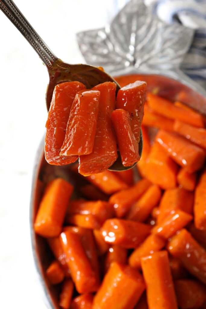 A spoon holds a serving of carrots over a bowl of brown sugar glazed carrots