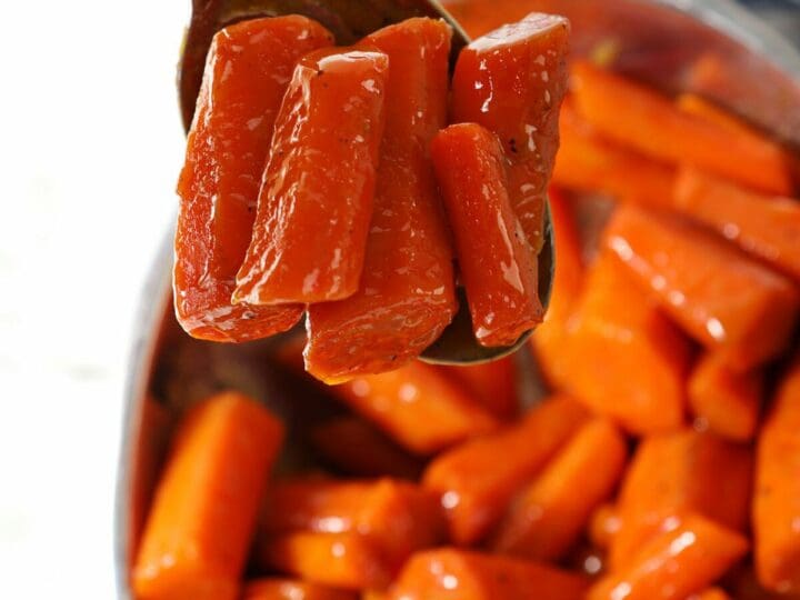 A spoon holds a serving of carrots over a bowl of brown sugar glazed carrots