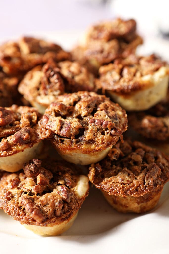 a stack of pecan tassie cookies on a white platter