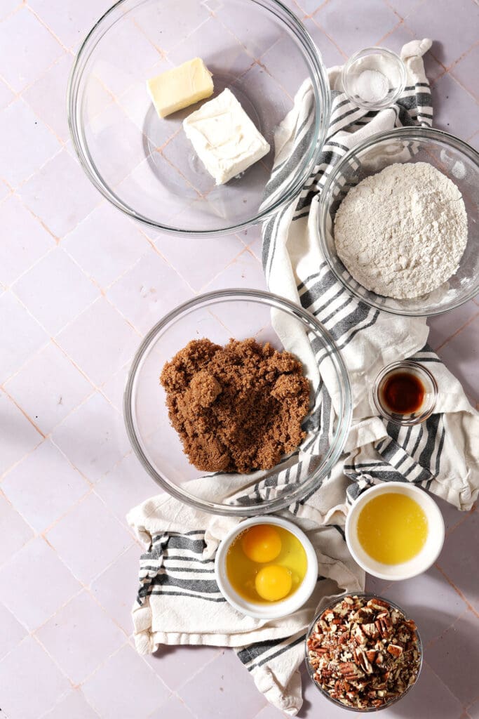 ingredients to make pecan tassies in bowls on a purple surface with a white and black striped towel