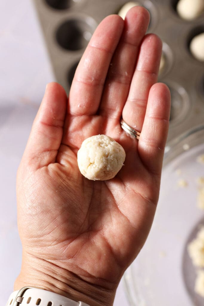 a ball of pie dough in the palm of a hand above a mini muffin tin